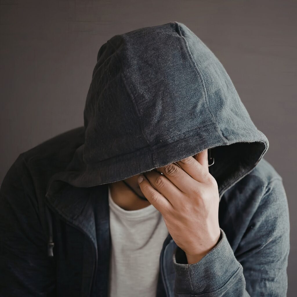 Man in hoodie, covering face with his hand